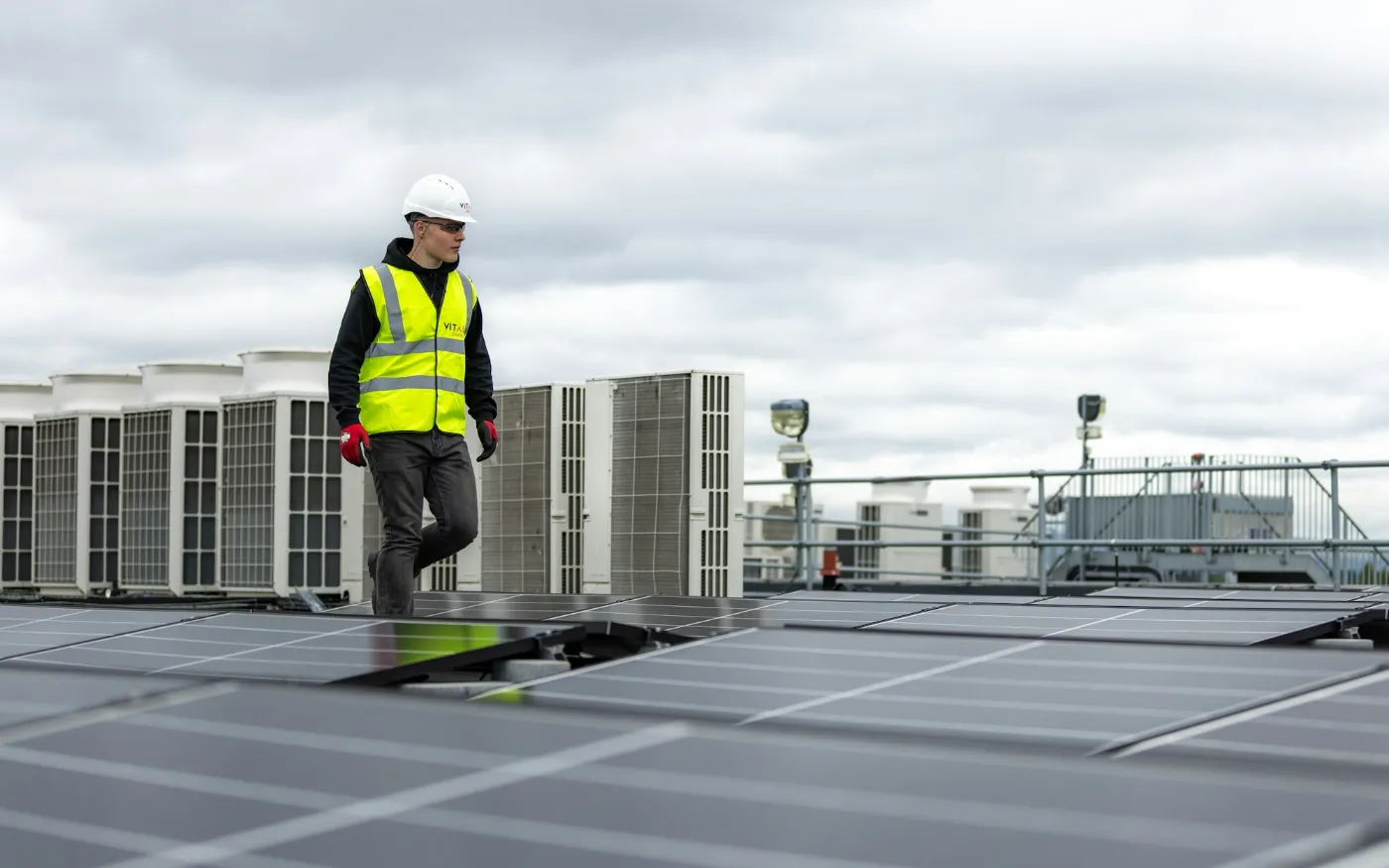 Technician in a safety vest walking past commercial rooftop HVAC units