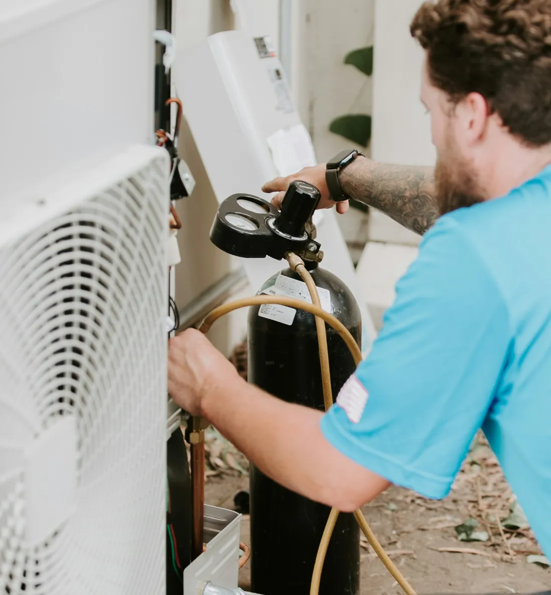 HVAC technician connecting refrigerant gauges to an outdoor air conditioning unit